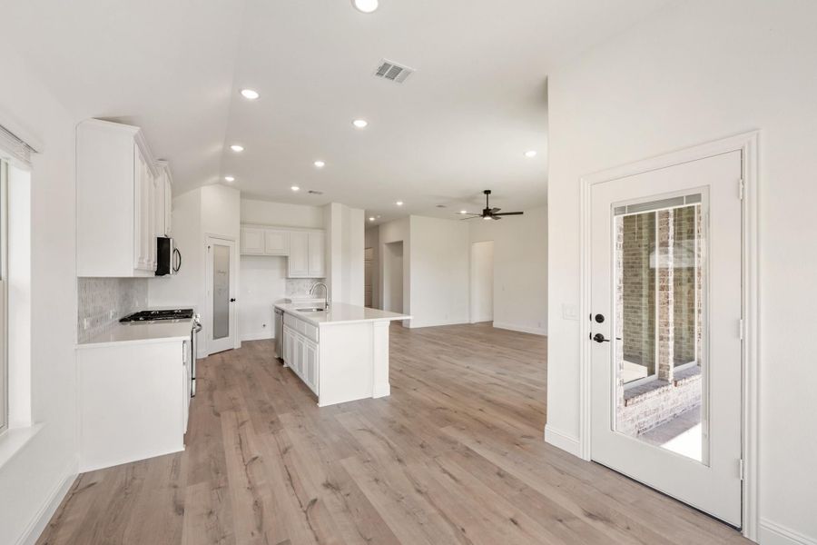 Open-concept kitchen with white cabinets, center island, and light wood floors leading to living area Open-concept kitchen with white cabinets, center island, and light wood floors leading to living area