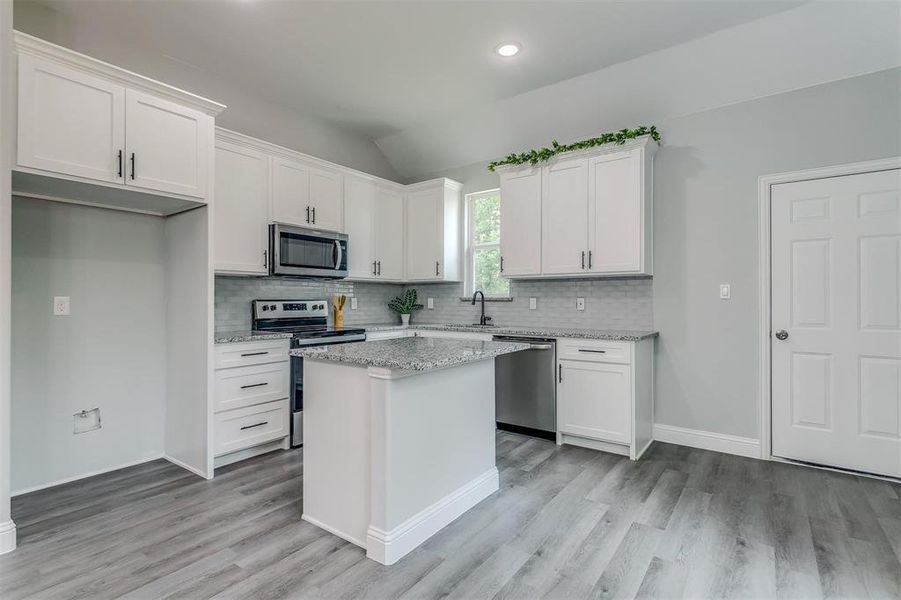 Kitchen with white cabinets, a center island, stainless steel appliances, and vaulted ceiling