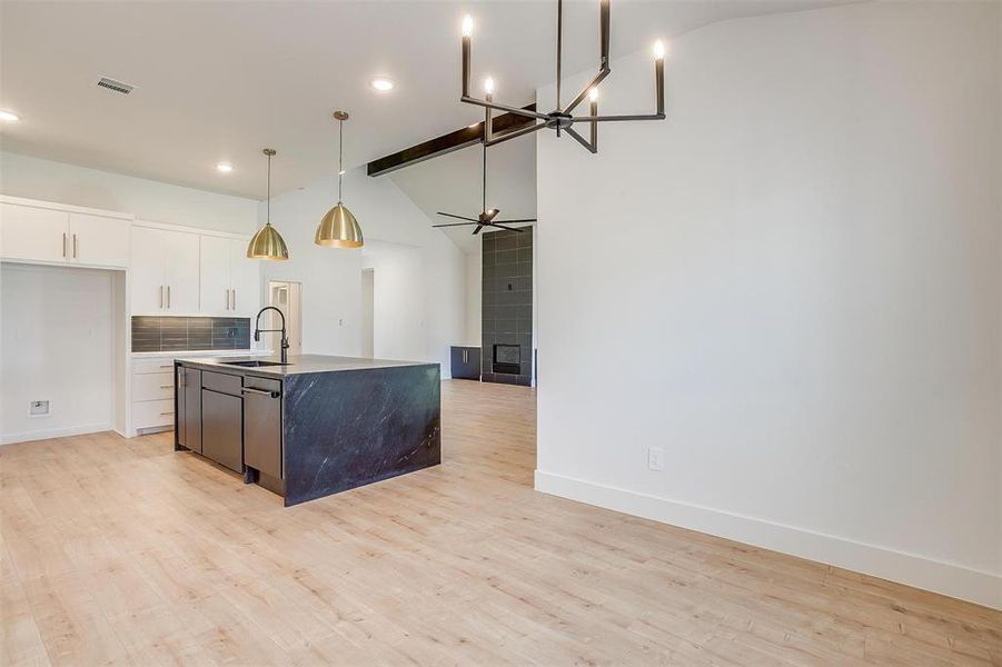 Kitchen with sink, light wood-type flooring, a center island with sink, and ceiling fan with notable chandelier