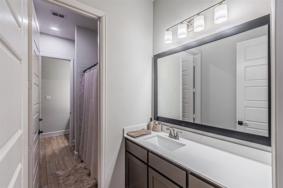 Bathroom vanity featuring a single basin sink, white countertop, and dark cabinetry