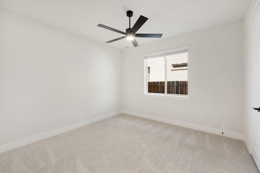 Empty bedroom with white walls, beige carpet, black ceiling fan, and single window
