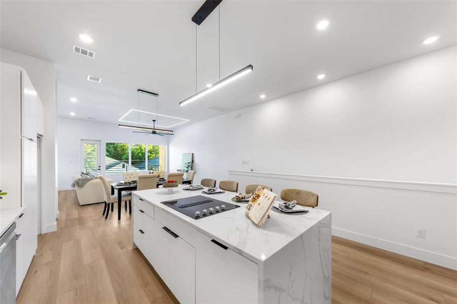 Kitchen featuring modern cabinets, black electric cooktop, white cabinets, a kitchen island, and light wood finished floors Kitchen featuring modern cabinets, black electric cooktop, white cabinets, a kitchen island, and light wood finished floors