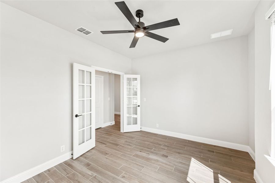Empty room with white French doors, wood-look tile floors, and a black ceiling fan