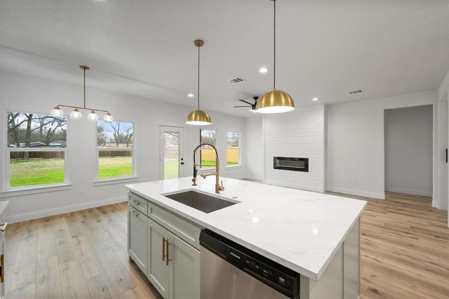 Kitchen featuring light stone counters, a fireplace, light wood-style floors, a sink, and dishwasher