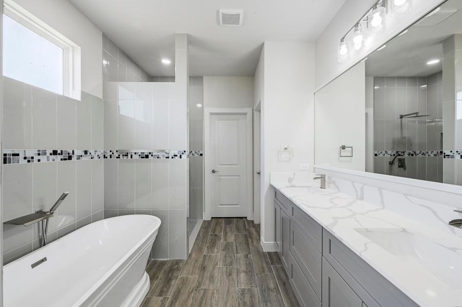 Full bath featuring a shower stall, a freestanding bath, double vanity, wood finished floors, and tile walls