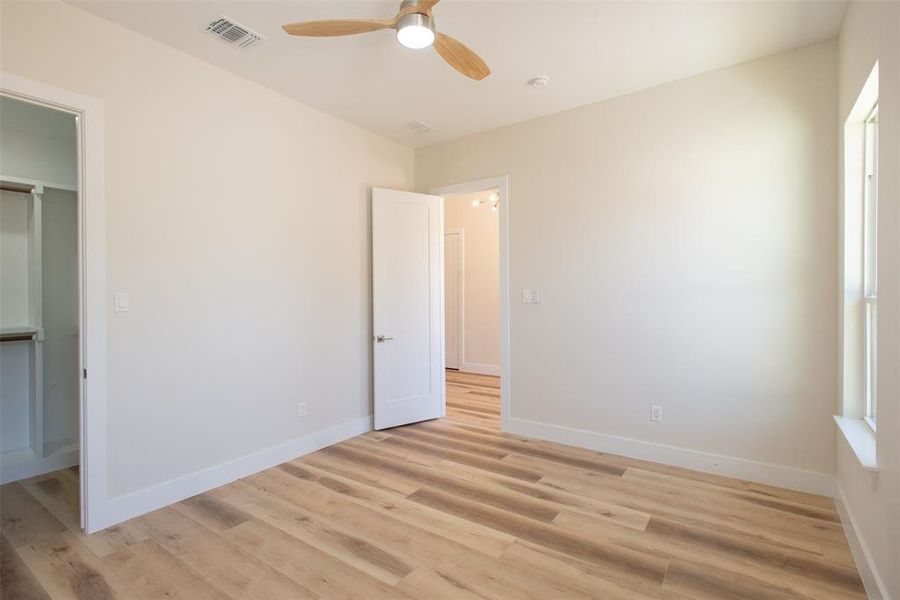 Unfurnished bedroom featuring a closet, light hardwood / wood-style floors, a spacious closet, and ceiling fan