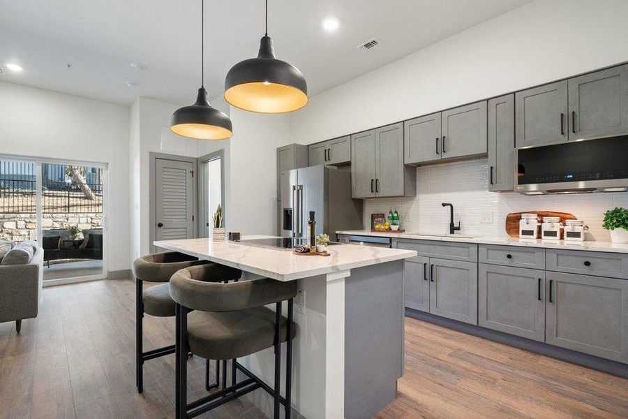 Kitchen with gray cabinets, a center island with sink, pendant lighting, light stone counters, and a high ceiling