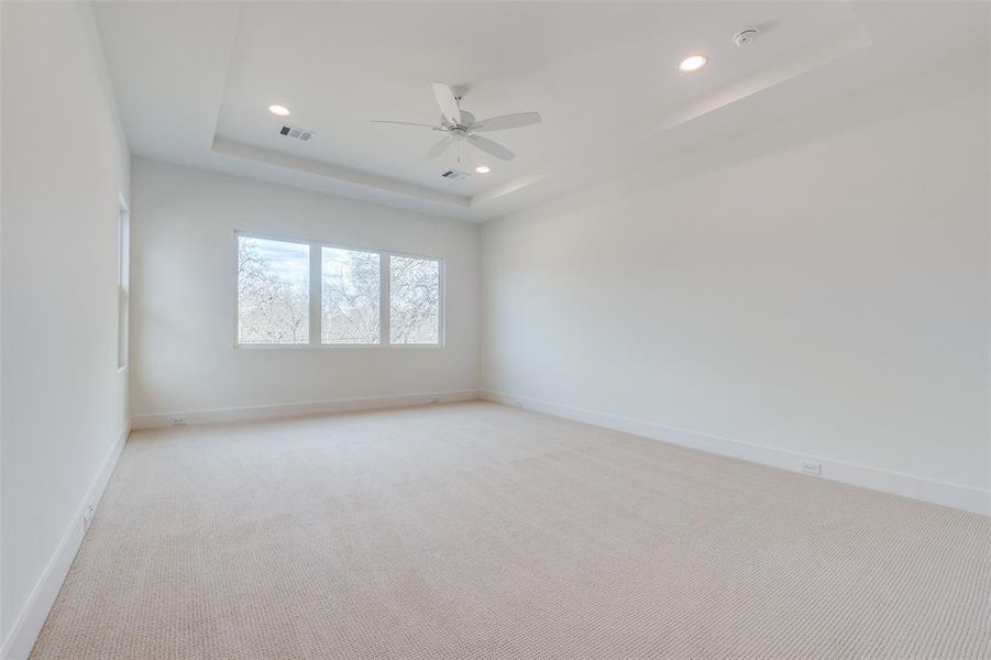 Carpeted empty room with ceiling fan and a tray ceiling