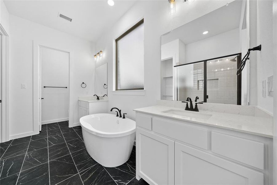 Bathroom featuring a freestanding soaking tub, dual vanity with white cabinetry and light-toned countertops, black-framed shower enclosure, and black tile flooring with white veining