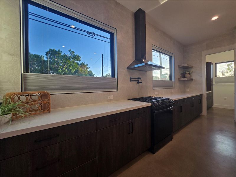 Streamlined cabinetry and sleek solid surfaces define this modern cooking space with large windows.
