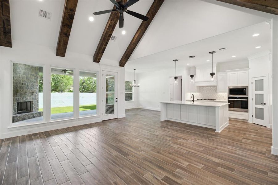 Kitchen featuring decorative light fixtures, stainless steel appliances, ceiling fan with notable chandelier, beam ceiling, and a center island with sink