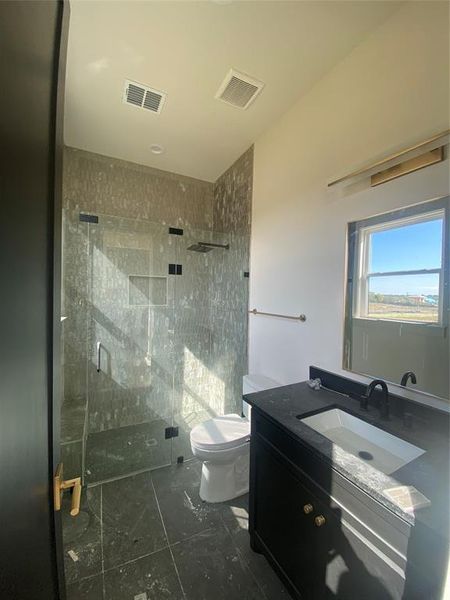 Bathroom featuring toilet, vanity, and a shower with shower door