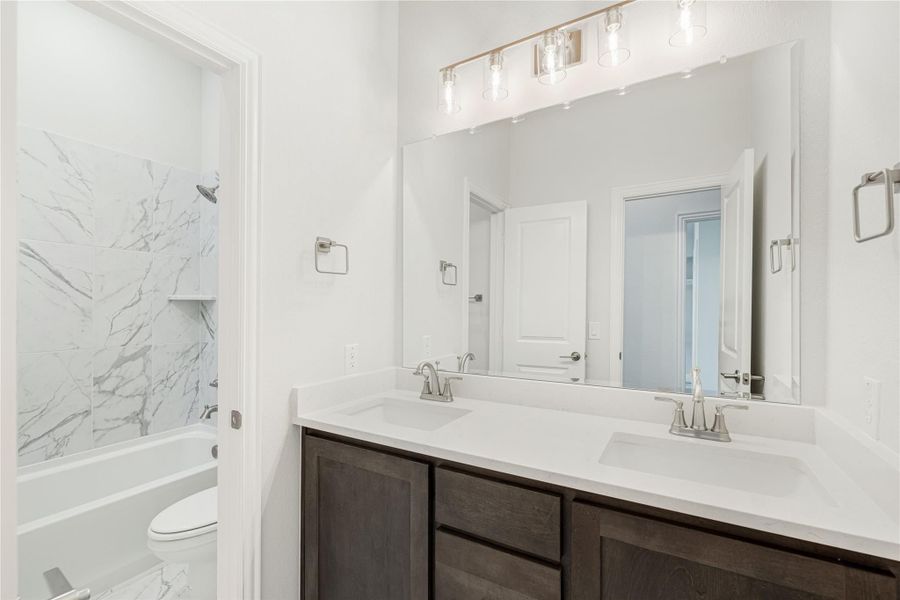 Bathroom with double sink vanity, dark wood cabinets, and marble tile tub-shower combo Bathroom with double sink vanity, dark wood cabinets, and marble tile tub-shower combo