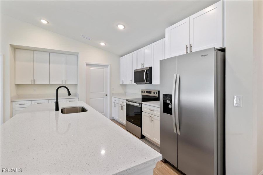 Kitchen with stainless steel appliances, white cabinets, light stone countertops, vaulted ceiling, and recessed lighting