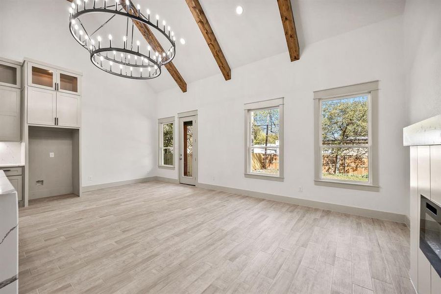 Unfurnished living room featuring high vaulted ceiling, light wood-type flooring, beam ceiling, a glass covered fireplace, and recessed lighting