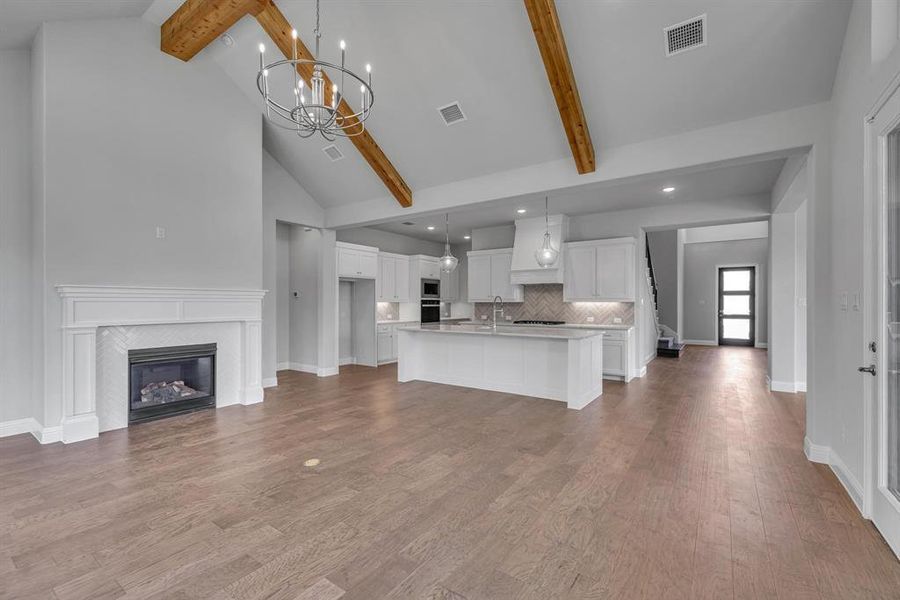 Kitchen with hanging light fixtures, custom range hood, light hardwood / wood-style flooring, beamed ceiling, and a center island with sink