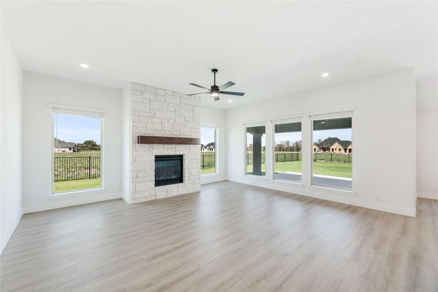 Open living room with stone fireplace, wood mantel, ceiling fan, and light hardwood floors