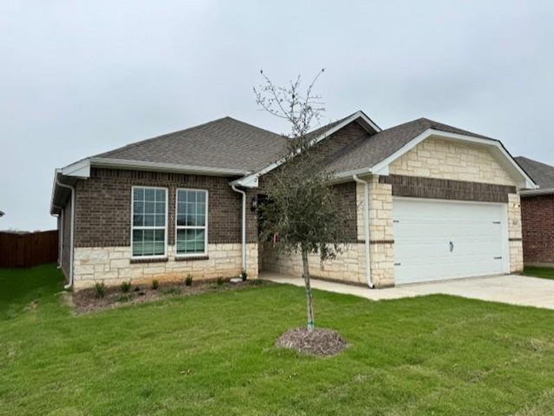 Single story home featuring an attached garage, a front lawn, roof with shingles, driveway, and stone siding Single story home featuring an attached garage, a front lawn, roof with shingles, driveway, and stone siding
