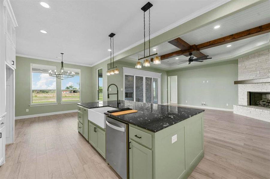 Kitchen featuring dishwasher, a stone fireplace, an island with sink, beamed ceiling, and light hardwood / wood-style floors