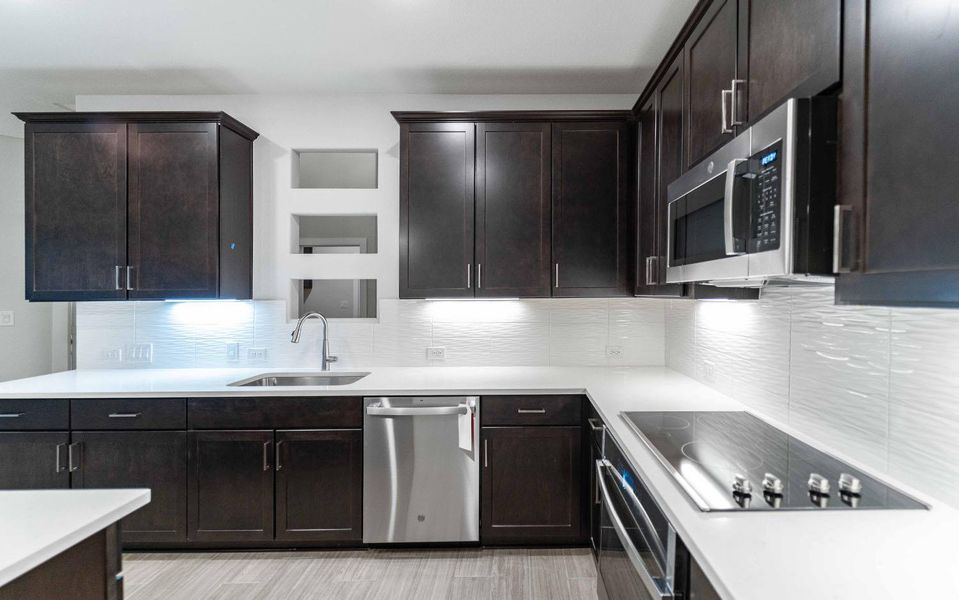 Kitchen featuring appliances with stainless steel finishes, light countertops, a sink, and tasteful backsplash