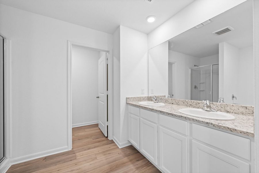 Full bath with a shower stall, double vanity, and light wood-style floors