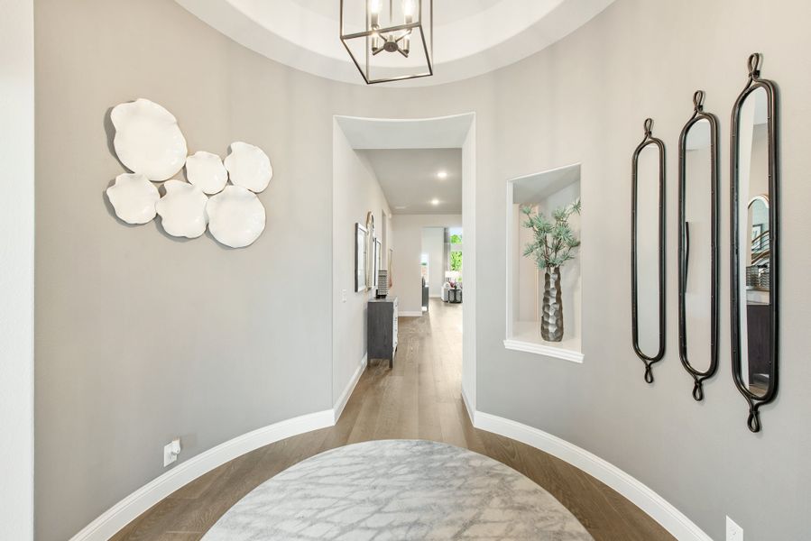 Rounded entryway with tray ceiling, pendant light, wall niche, and hardwood floors leading to hallway Rounded entryway with tray ceiling, pendant light, wall niche, and hardwood floors leading to hallway