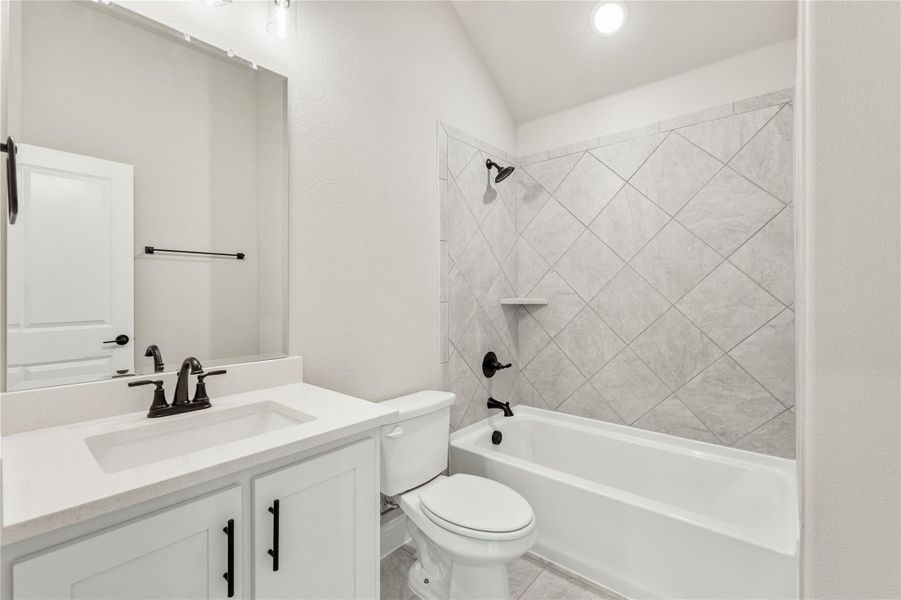 Bathroom with white vanity, toilet, and tub-shower combo with diagonal tile surround and dark bronze fixtures Bathroom with white vanity, toilet, and tub-shower combo with diagonal tile surround and dark bronze fixtures