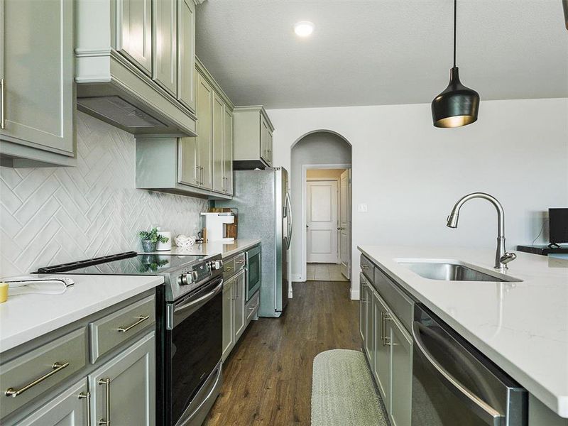 Kitchen featuring decorative light fixtures, dark hardwood / wood-style flooring, stainless steel appliances, tasteful backsplash, and sink