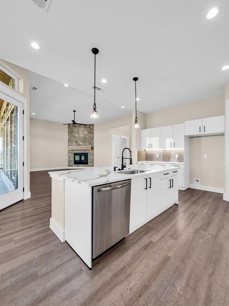 Kitchen featuring white cabinetry, stainless steel dishwasher, light wood-type flooring, and a large island with sink