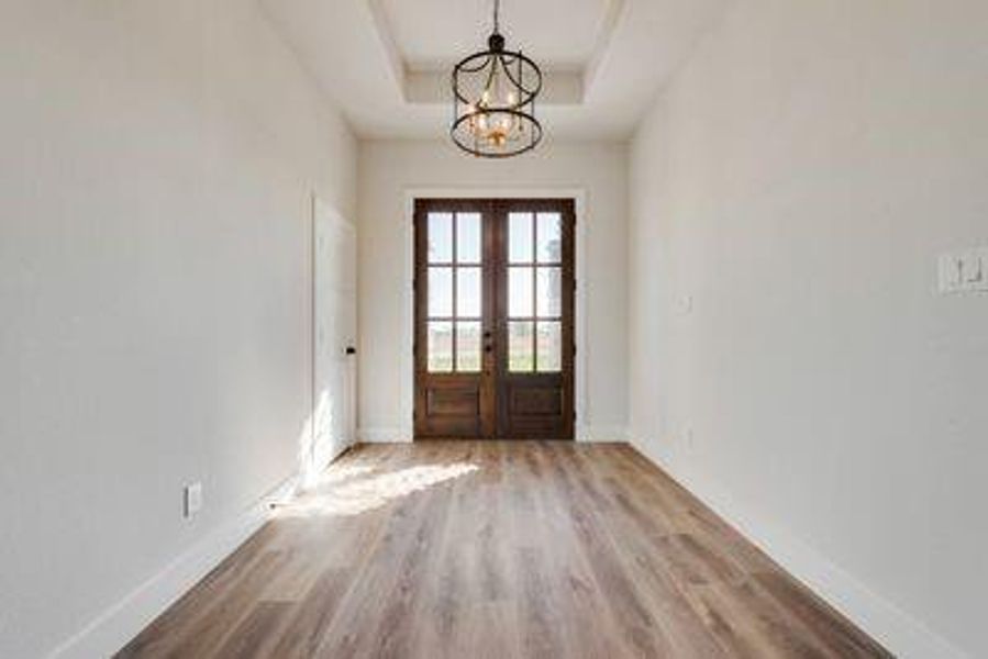 Doorway featuring light hardwood / wood-style floors, french doors, an inviting chandelier, and a raised ceiling