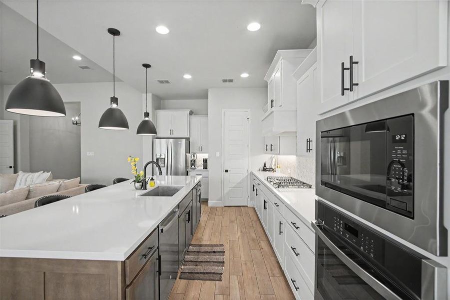 Spacious kitchen featuring an expansive island with a stainless steel sink and matte black faucet, pendant lighting, white cabinetry, and wood-finish flooring