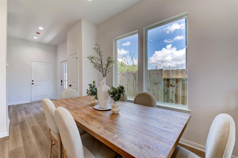 Dining room with hardwood floors, high ceilings, recessed lighting, dual large windows with backyard views, and open sightline to front entry door.