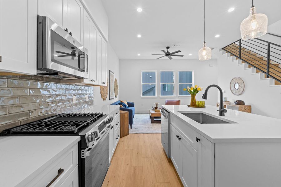 Kitchen with open floor plan, stainless steel appliances, ceiling fan, light wood finished floors, and hanging light fixtures