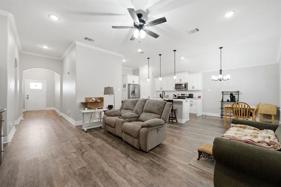 Living room with a chandelier, crown molding, dark wood-style flooring, arched walkways, and ceiling fan