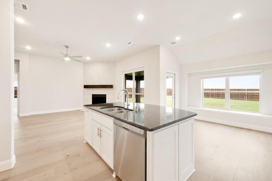 Kitchen island with dark granite countertop, sink, and dishwasher, open to living area with fireplace and light wood floors