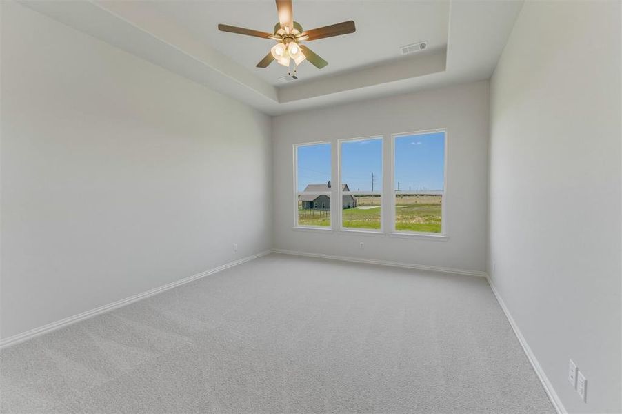 Spacious room featuring three large windows, a tray ceiling, and a ceiling fan with integrated lighting