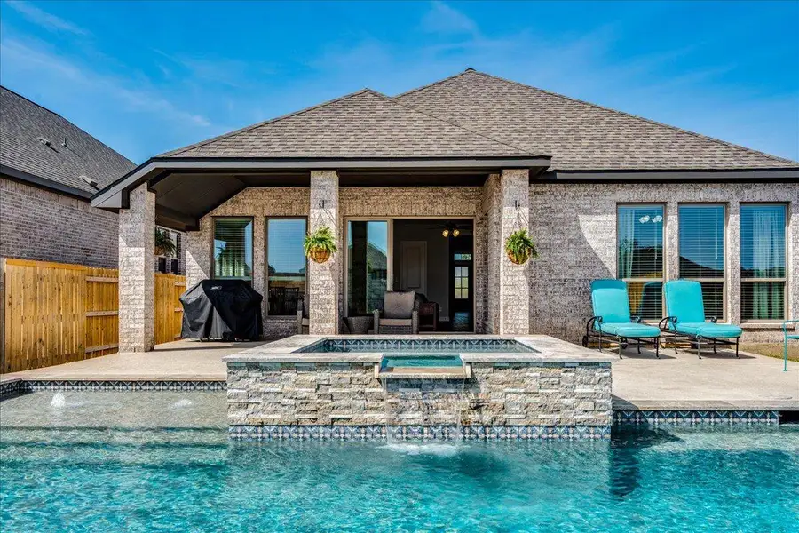 Rear view of property featuring roof with shingles, a patio area, brick siding, and a pool with connected hot tub