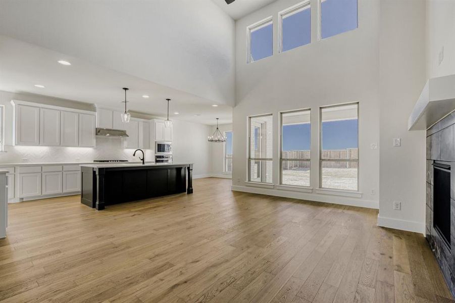 Dual tone kitchen with a tile fireplace, open floor plan, light countertops, an island with sink, and hanging lights