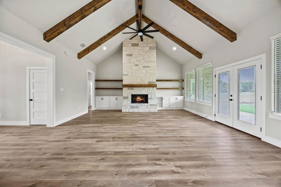 Unfurnished living room with light wood-style flooring, french doors, high vaulted ceiling, recessed lighting, and a stone fireplace Unfurnished living room with light wood-style flooring, french doors, high vaulted ceiling, recessed lighting, and a stone fireplace