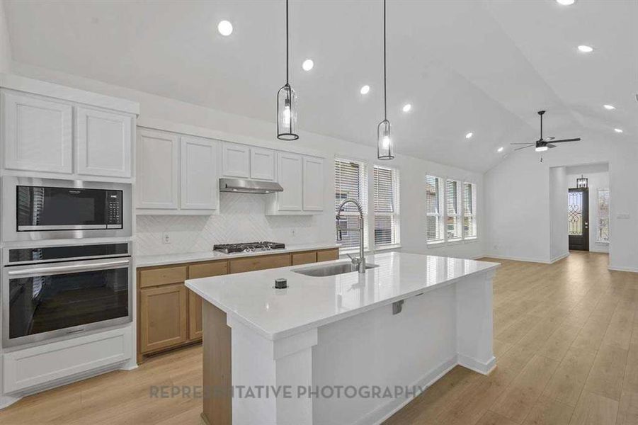 Kitchen with stainless steel appliances, white cabinets, light wood finished floors, tasteful backsplash, and lofted ceiling
