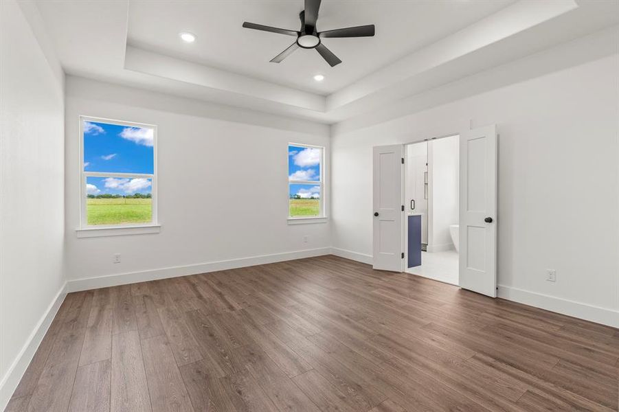 Unfurnished bedroom with a tray ceiling, dark wood finished floors, recessed lighting, connected bathroom, and ceiling fan