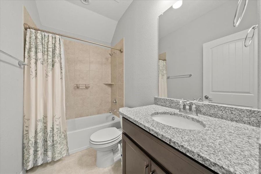 Full Hallway bathroom with shower / bath combination with curtain, tile patterned floors, vanity, toilet, and lofted ceiling.