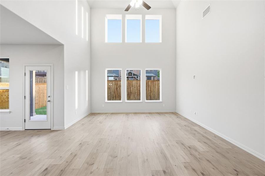 Unfurnished living room featuring light wood-style flooring, ceiling fan, and a towering ceiling