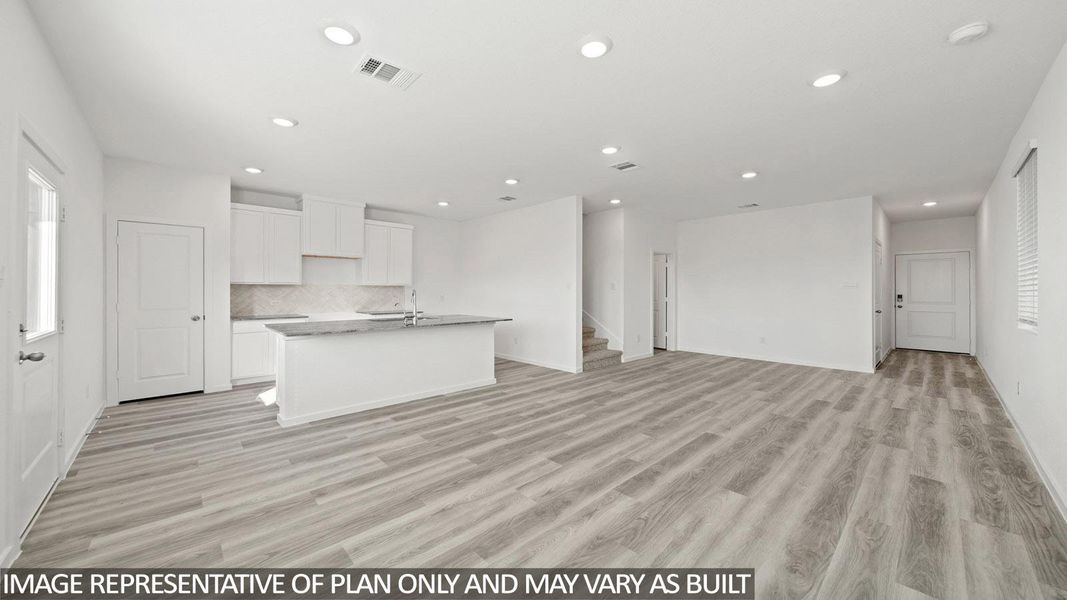 Expansive open-concept living area featuring light wood-finish flooring, a contemporary kitchen island with seating, recessed lighting, and white cabinetry