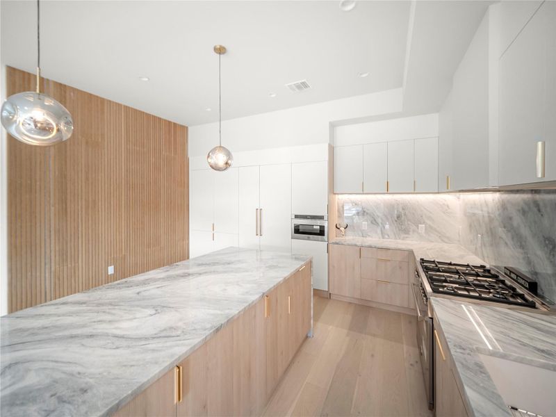Dual tone kitchen featuring two tone color scheme, light stone counters, modern cabinets, light wood-type flooring, and stainless steel appliances