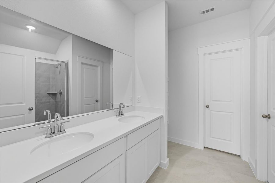 Full bath featuring a shower stall, double vanity, and light tile patterned floors