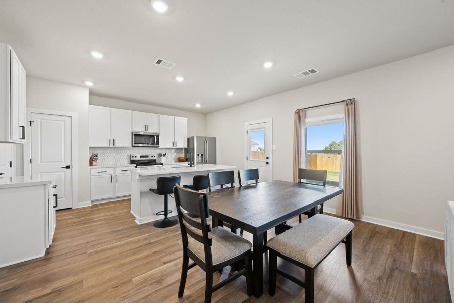 An open dining area flows seamlessly into a contemporary kitchen with wood-look flooring. An open dining area flows seamlessly into a contemporary kitchen with wood-look flooring.