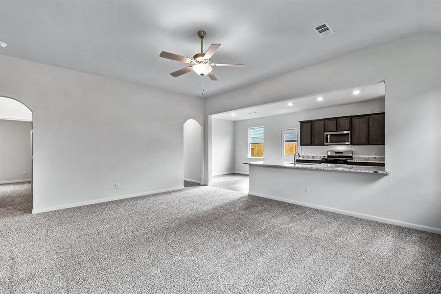 Kitchen featuring appliances with stainless steel finishes, light carpet, light stone counters, dark brown cabinets, and ceiling fan