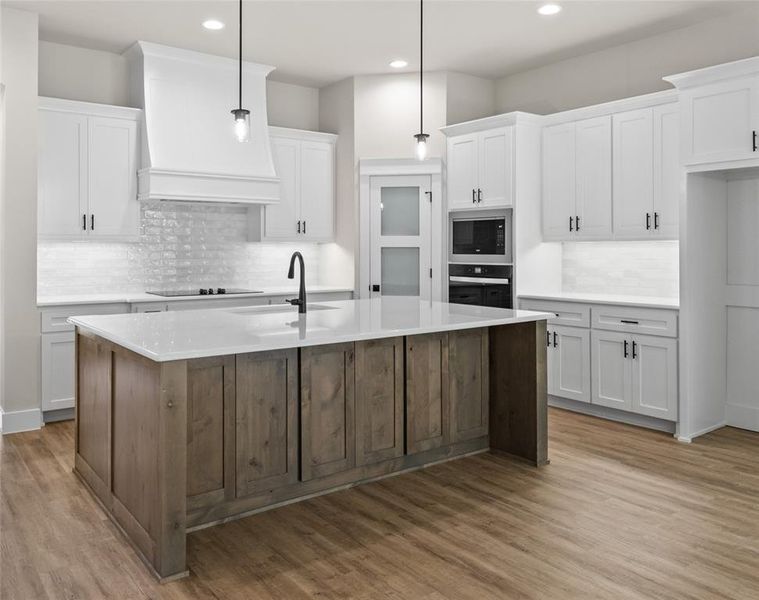 Kitchen featuring two tone cabinetry, a kitchen island with sink, dark wood-style floors, tasteful backsplash, and built in microwave