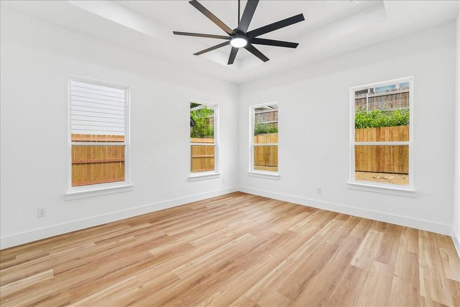 Spacious room featuring light wood-finish flooring, white walls, and a contemporary ceiling fan Spacious room featuring light wood-finish flooring, white walls, and a contemporary ceiling fan